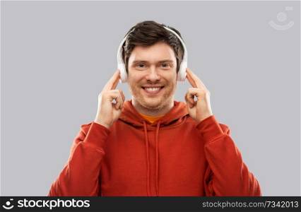 music, technology and people concept - happy young man in headphones and red hoodie over grey background. happy young man in headphones and red hoodie