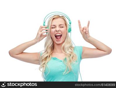 music, technology and people concept - happy young woman or teenage girl with headphones singing song and showing rock gesture