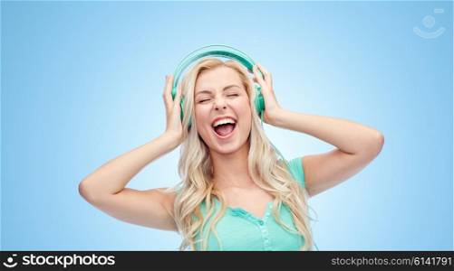music, technology and people concept - happy young woman or teenage girl with headphones singing song over blue background