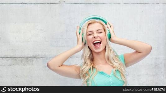 music, technology and people concept - happy young woman or teenage girl with headphones singing song over gray concrete wall background