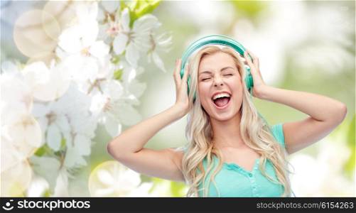 music, technology and people concept - happy young woman or teenage girl with headphones singing song over natural spring cherry blossom background