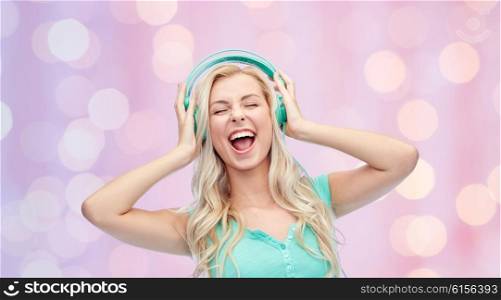 music, technology and people concept - happy young woman or teenage girl with headphones singing song over pink holidays lights background
