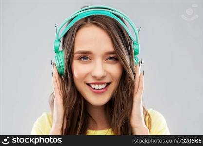 music, technology and people concept - happy young woman or teenage girl with headphones over grey background. happy young woman or teenage girl with headphones