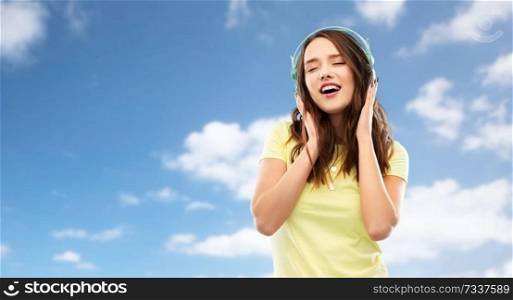 music, technology and people concept - happy young woman or teenage girl with headphones over blue sky and clouds background. happy young woman or teenage girl with headphones