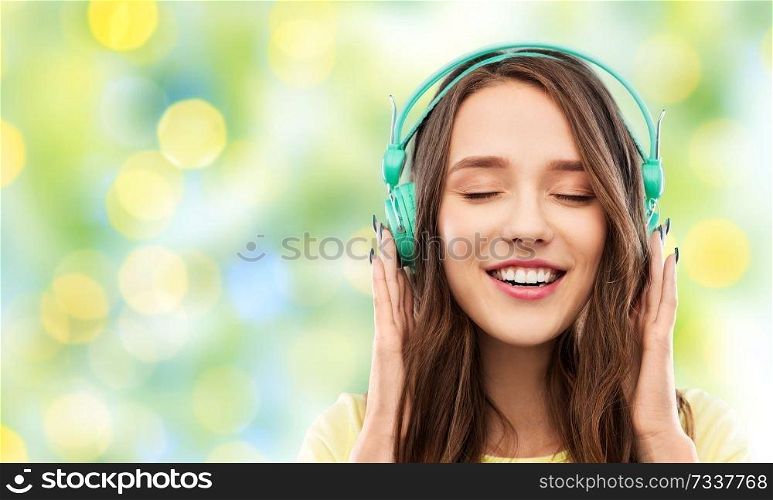 music, technology and people concept - happy young woman or teenage girl with headphones over summer green lights background. happy young woman or teenage girl with headphones