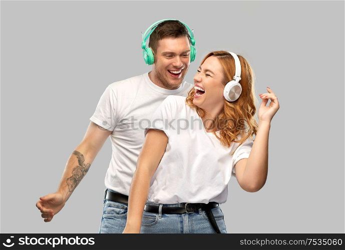 music, technology and people concept - portrait of happy couple in white t-shirts and headphones dancing over grey background. happy couple in headphones dancing