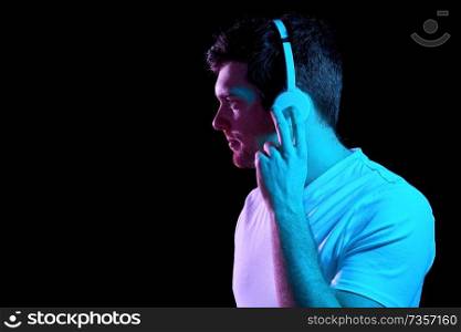 music, technology and people concept - portrait of young man in wireless headphones over ultra violet neon lights in dark room of night club. man in headphones over neon lights of night club