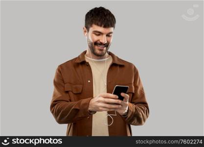 music, technology and people concept - smiling young man with earphones and smartphone over grey background. smiling young man with earphones and smartphone
