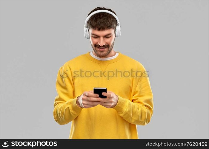 music, technology and people concept - smiling young man with headphones and smartphone over grey background. smiling young man with headphones and smartphone