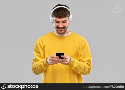 music, technology and people concept - smiling young man with headphones and smartphone over grey background. smiling young man with headphones and smartphone
