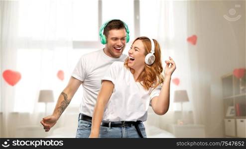 music, technology and valentine&rsquo;s day concept - portrait of happy couple in white t-shirts and headphones dancing over bedroom decorated with heart shaped balloons background. happy couple in headphones dancing