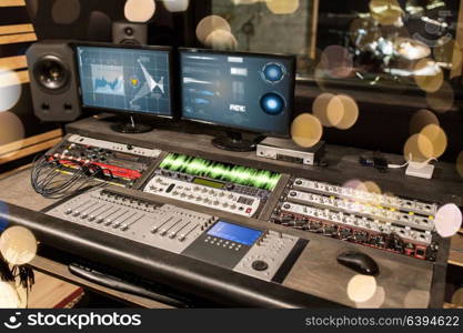 music, technology, electronics and equipment concept - mixing console and computer monitors at sound recording studio over lights. music mixing console at sound recording studio