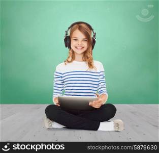 music, technology, people and childhood concept - happy girl with headphones and tablet pc computer over green chalk board background