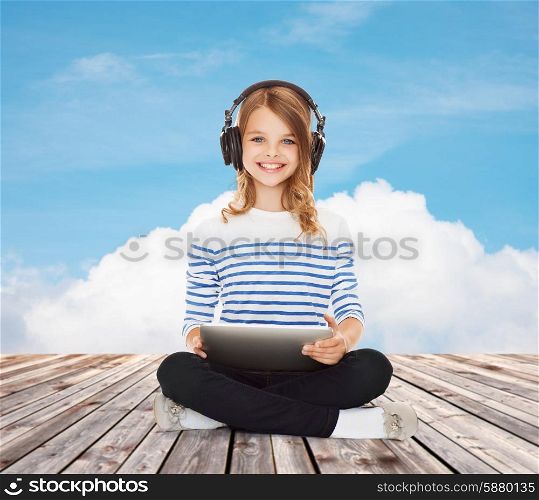 music, technology, people and childhood concept - happy girl with headphones and tablet pc computer over blue sky and cloud background