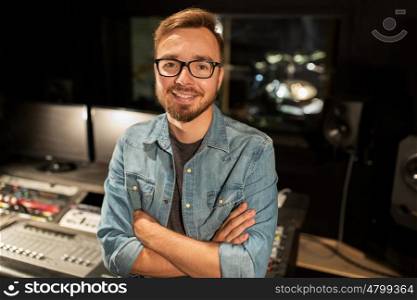music, technology, people and equipment concept - happy smiling man at mixing console in sound recording studio