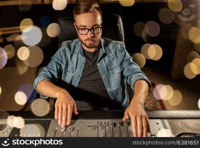 music, technology, people and equipment concept - man at mixing console in sound recording studio over lights. man at mixing console in music recording studio