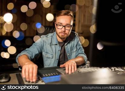 music, technology, people and equipment concept - man at mixing console in sound recording studio over festive lights. man at mixing console in music recording studio