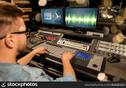 music, technology, people and equipment concept - man at mixing console in sound recording studio over festive lights. man at mixing console in music recording studio