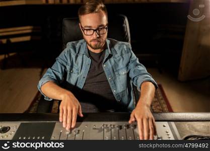 music, technology, people and equipment concept - man at mixing console in sound recording studio