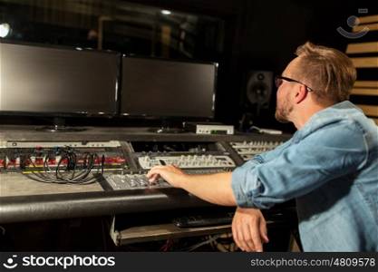 music, technology, people and equipment concept - man at mixing console in sound recording studio. man at mixing console in music recording studio