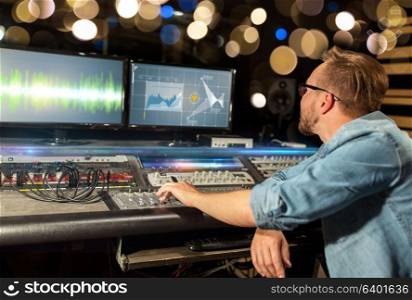 music, technology, people and equipment concept - man at mixing console with computer monitors in sound recording studio over festive lights. man at mixing console in music recording studio