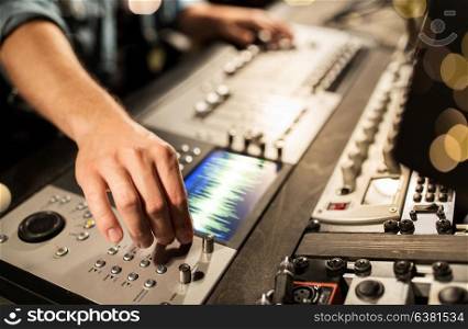 music, technology, people and equipment concept - man using mixing console in sound recording studio over lights. man using mixing console in music recording studio