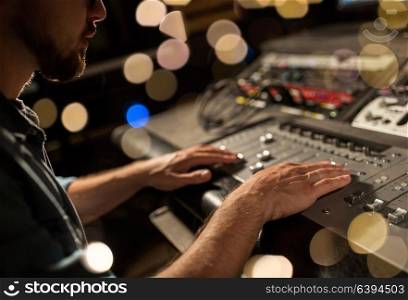 music, technology, people and equipment concept - man using mixing console in sound recording studio over lights. man using mixing console in music recording studio