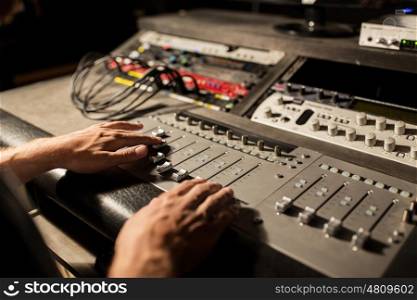 music, technology, people and equipment concept - man using mixing console in sound recording studio. man using mixing console in music recording studio