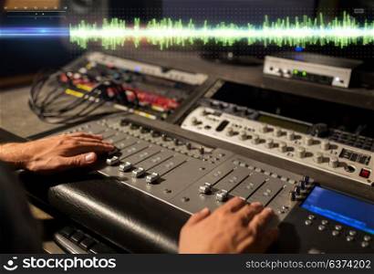 music, technology, people and equipment concept - sound engineer hands using mixing console at recording studio. hands on mixing console at sound recording studio