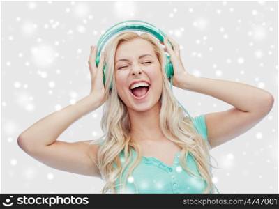 music, technology, winter holidays, christmas and people concept - happy young woman or teenage girl with headphones singing song over snow