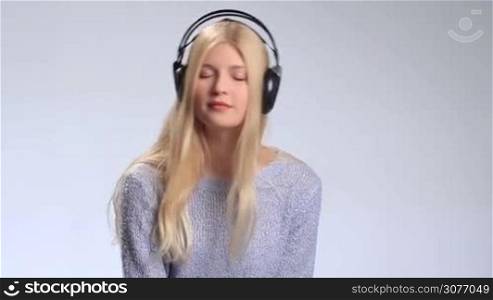 Music teenager girl with closed eyes listening to favorite song with headphones on white background. Young attractive woman enjoying music, opening her eyes, confusedly smiling at the camera and then closing her eyes again and moving groovily to the beat.