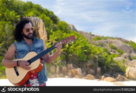 music, travel and people concept - young hippie man playing guitar and singing over tropical island beach background. hippie man playing guitar over island beach