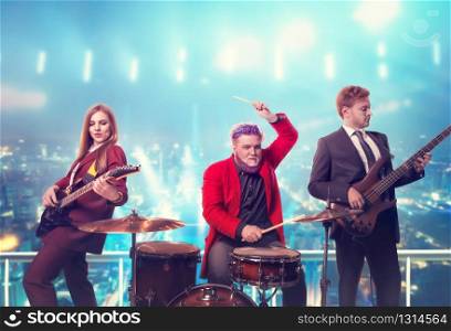 Musical group in suits, performing on the rooftop, retro style, night cityscape on background. Guitarists and drummer, rock band