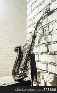 Musical woodwind instrument saxophone with old briefcase on the brick wall background. Vintage stylized monochrome toned concept image with space for copy and design.
