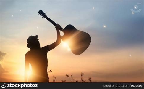 Musician holding guitar in hand of silhouette on sunset nature background