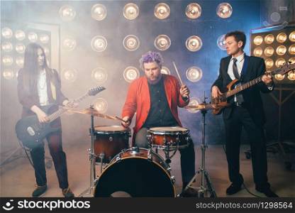 Musicians in suits on the stage with lights, vintage style. Guitarists and drummer, rock band concert, music show