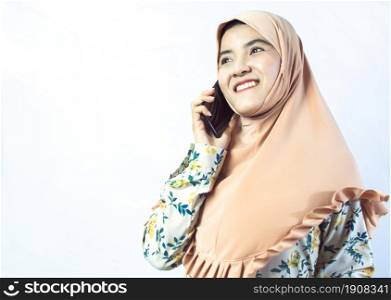 Muslim business woman wearing hijab and talking mobile phone while standing on white background. Technology and Religion Concept.