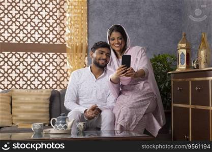 Muslim couple taking selfie together while sitting on sofa at home
