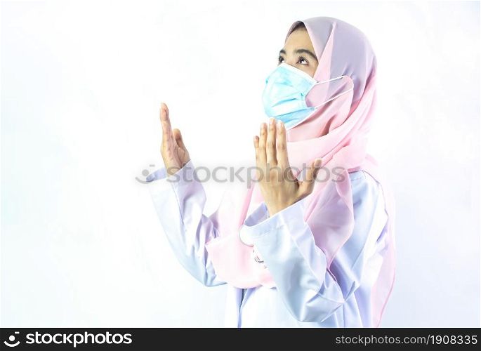 Muslim female doctor with hijab wearing mask and praying to protect virus and illness. Medical and Religion Concept.