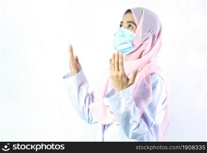 Muslim female doctor with hijab wearing mask and praying to protect virus and illness. Medical and Religion Concept.