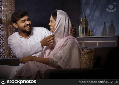 Muslim man looking at his beautiful wife while sitting on sofa in living room