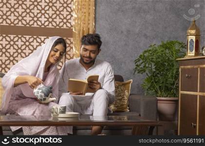 Muslim woman making tea in living room while her husband reading a book
