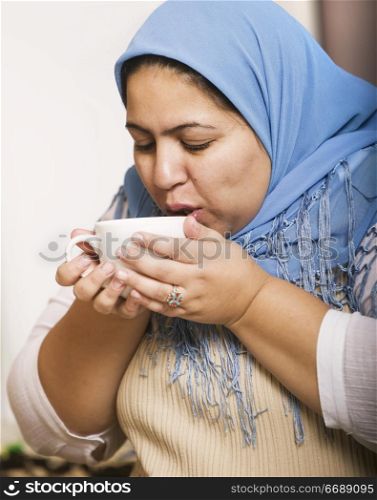 Muslim woman wearing a head scarf drinking coffee
