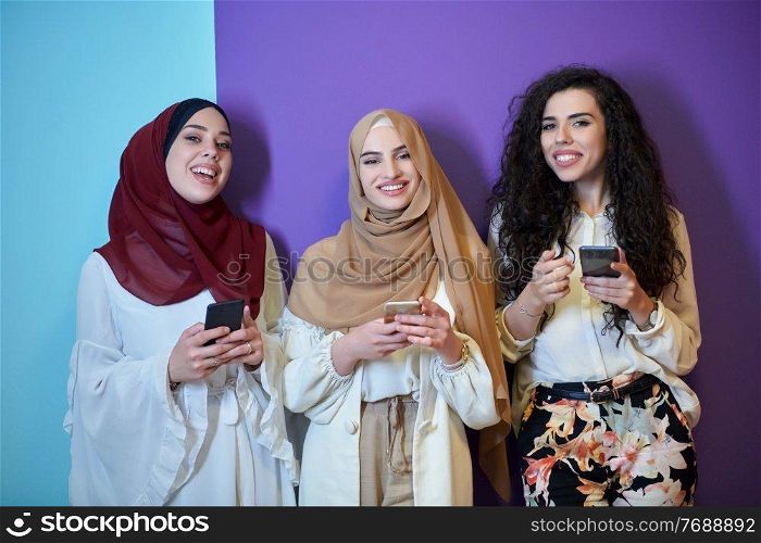 Muslim women using mobile phones isolated on blue and purple background. Young and happy Arabic girls while chatting or searching on the internet, browsing