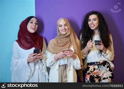 Muslim women using mobile phones isolated on blue and purple background. Young and happy Arabic girls while chatting or searching on the internet, browsing