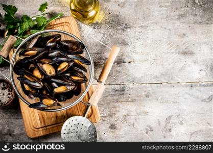 Mussels in a colander on a cutting board with parsley. On a gray background. High quality photo. Mussels in a colander on a cutting board with parsley.