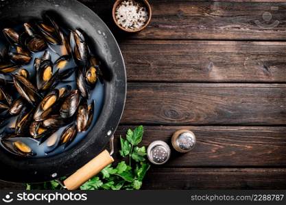 Mussels in a saucepan with parsley and spices. On a wooden background. High quality photo. Mussels in a saucepan with parsley and spices.