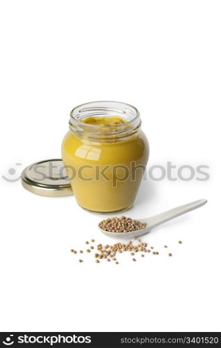 Mustard in a jar and mustard seeds on a spoon on white background