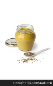 Mustard in a jar and mustard seeds on a spoon on white background