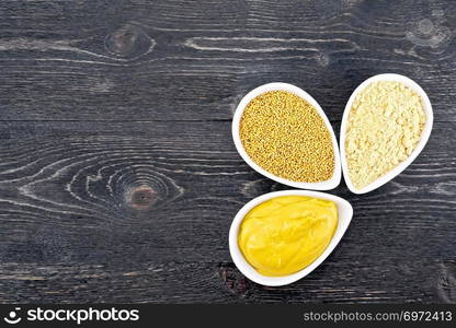 Mustard sauce, seeds and mustard powder in three saucepans on a wooden plank background